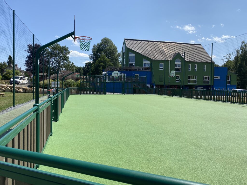 Terrain de basket extérieur, école verte, jour ensoleillé.