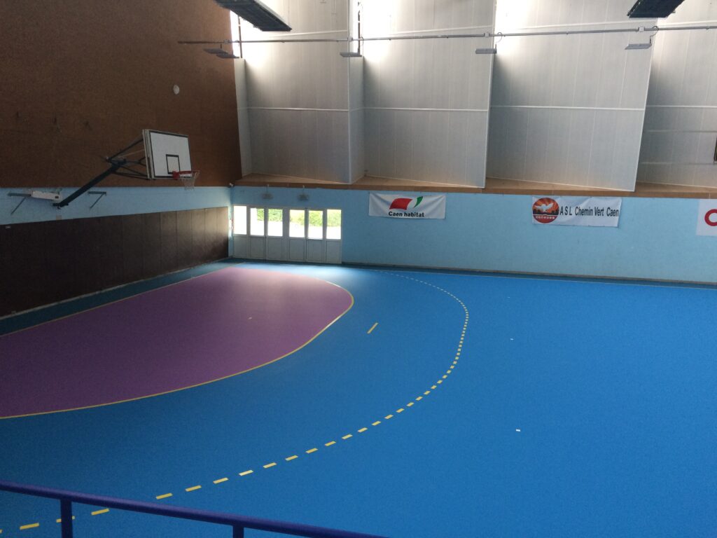 Gymnase vide avec terrain de basket et logos sponsors.