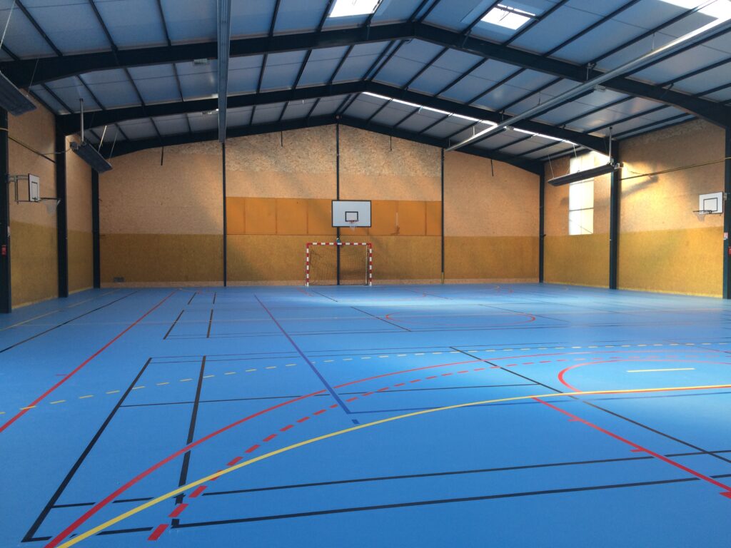 Gymnase vide avec terrains de sport marqués.