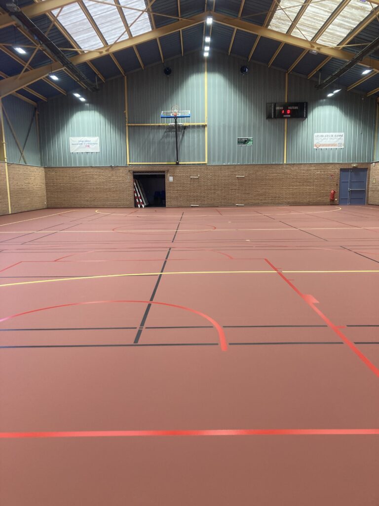 Gymnase intérieur avec terrains de sport marqués.