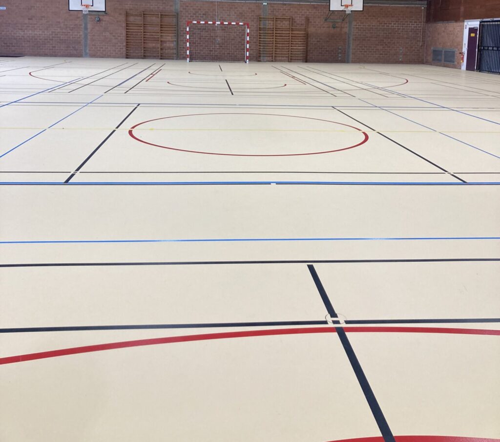 Gymnase intérieur vide avec terrains de sport marqués.