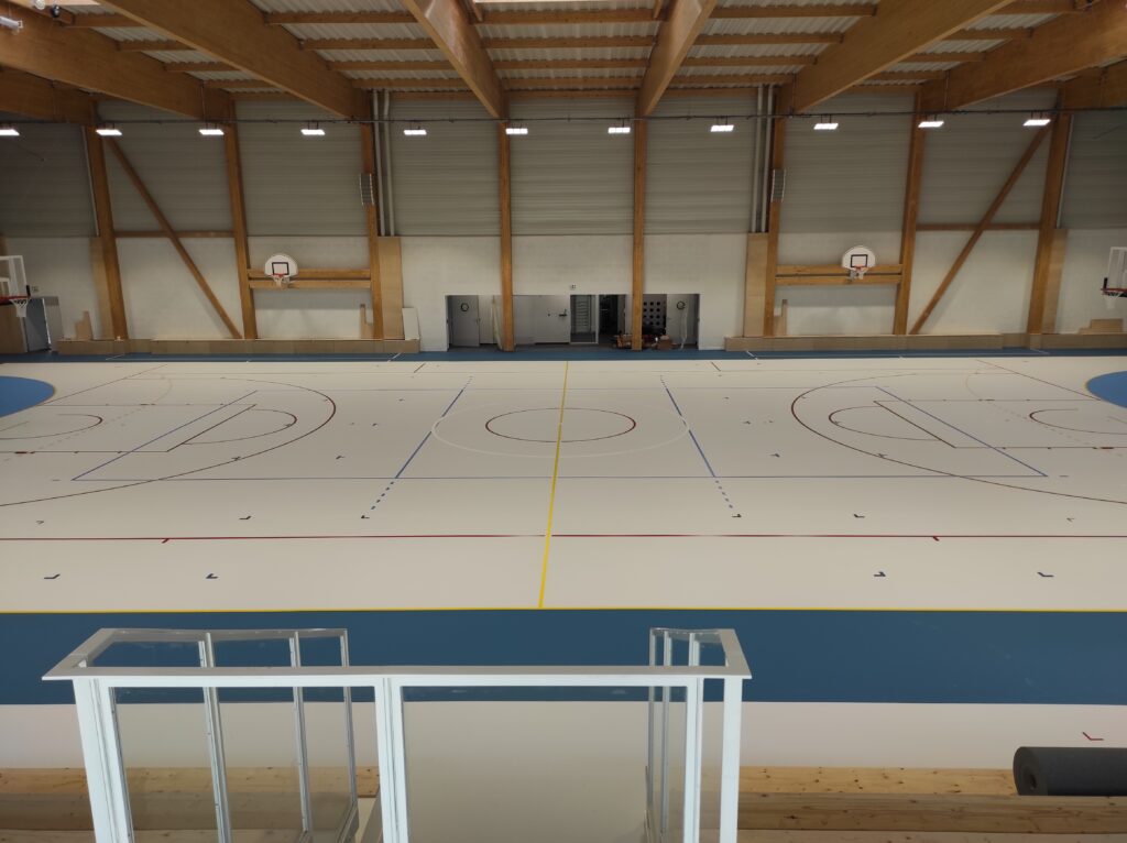 Gymnase vide avec terrains de sport marqués.