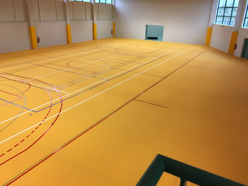 Gymnase vide avec marquages au sol colorés.