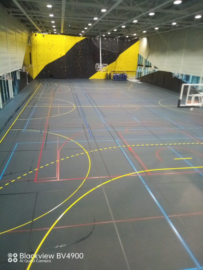 Salle de sport avec terrains multisports et mur d'escalade.