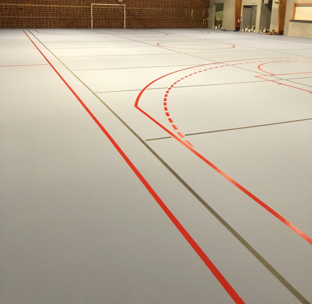 Gymnase vide avec terrain de basket marqué.