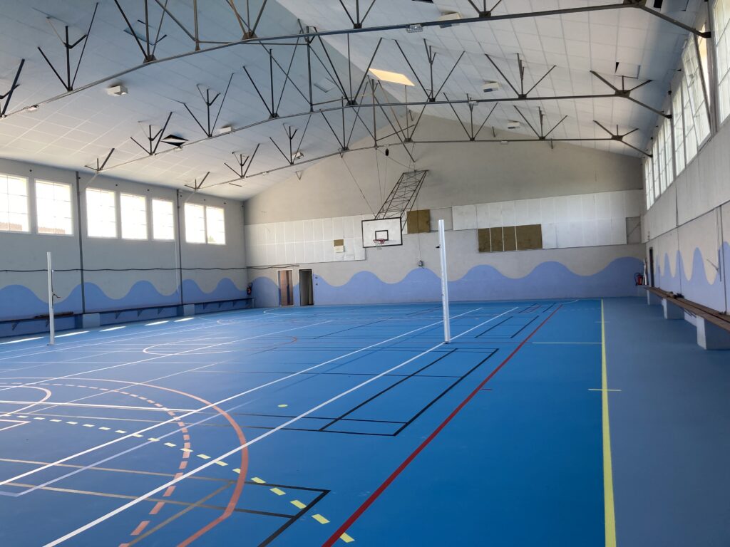 Gymnase vide avec terrains de sport marqués au sol.