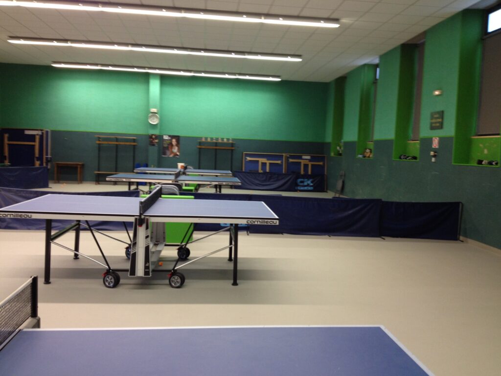 Salle de ping-pong intérieure avec tables et filets.