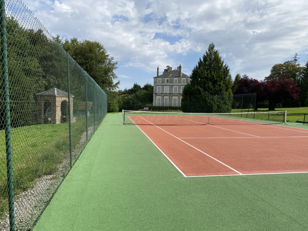 Terrain de tennis extérieur et manoir en arrière-plan.