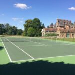 Terrain de tennis et manoir en arrière-plan.