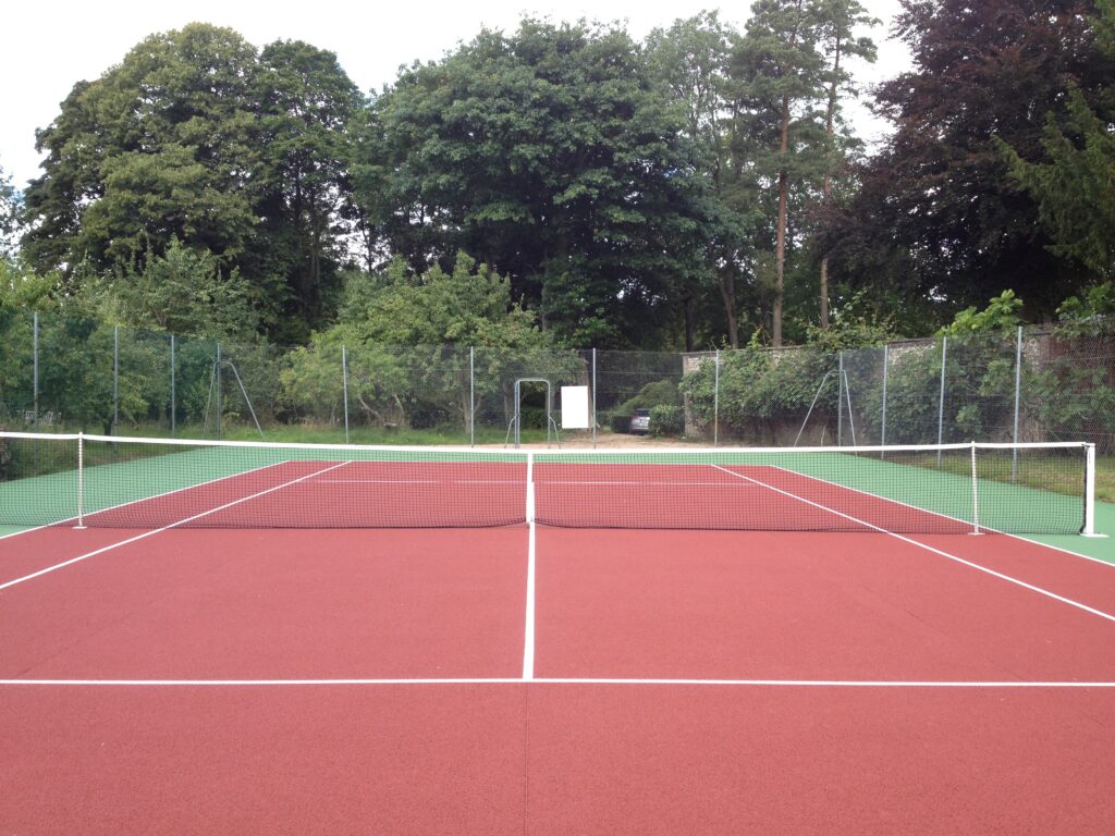 Terrain de tennis extérieur, filet, arbres en arrière-plan.