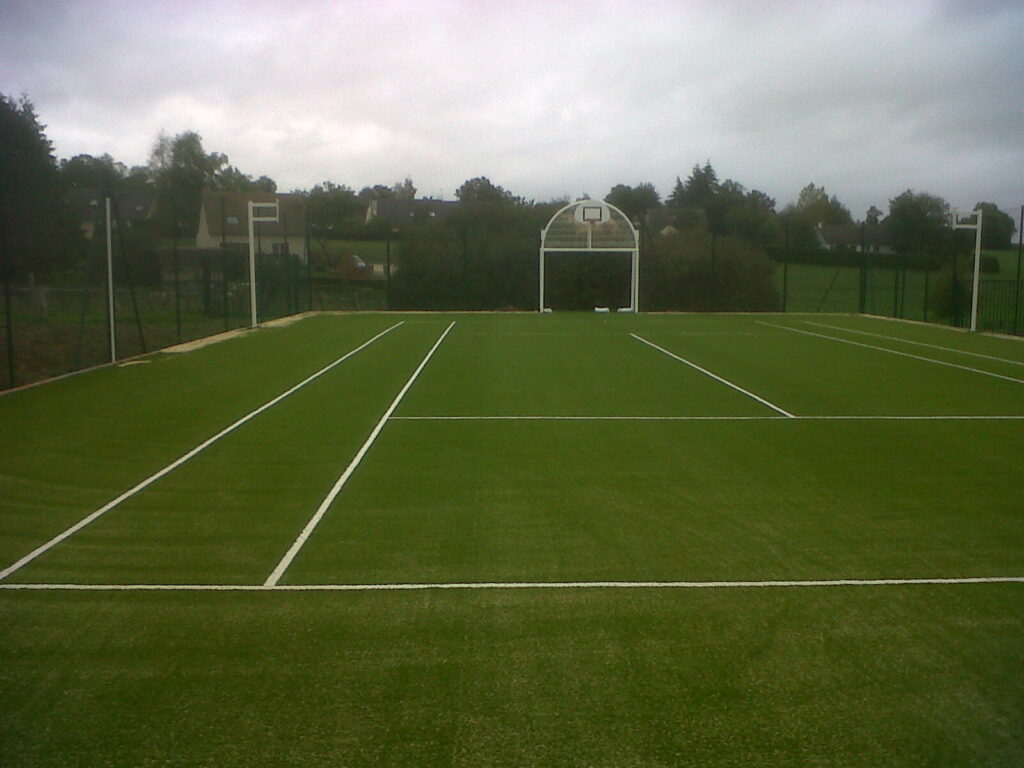 Terrain de tennis extérieur, lignes blanches, gazon synthétique.