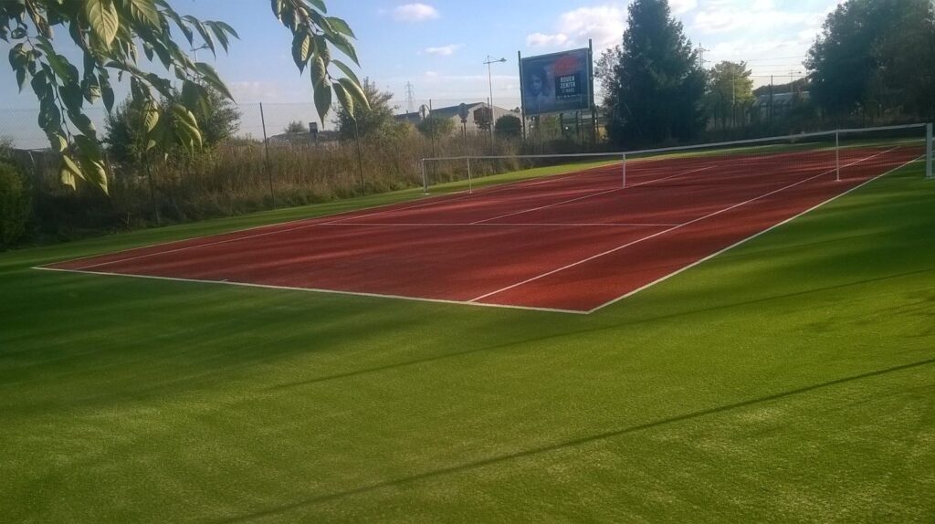 Terrain de tennis extérieur, sol rouge et vert.