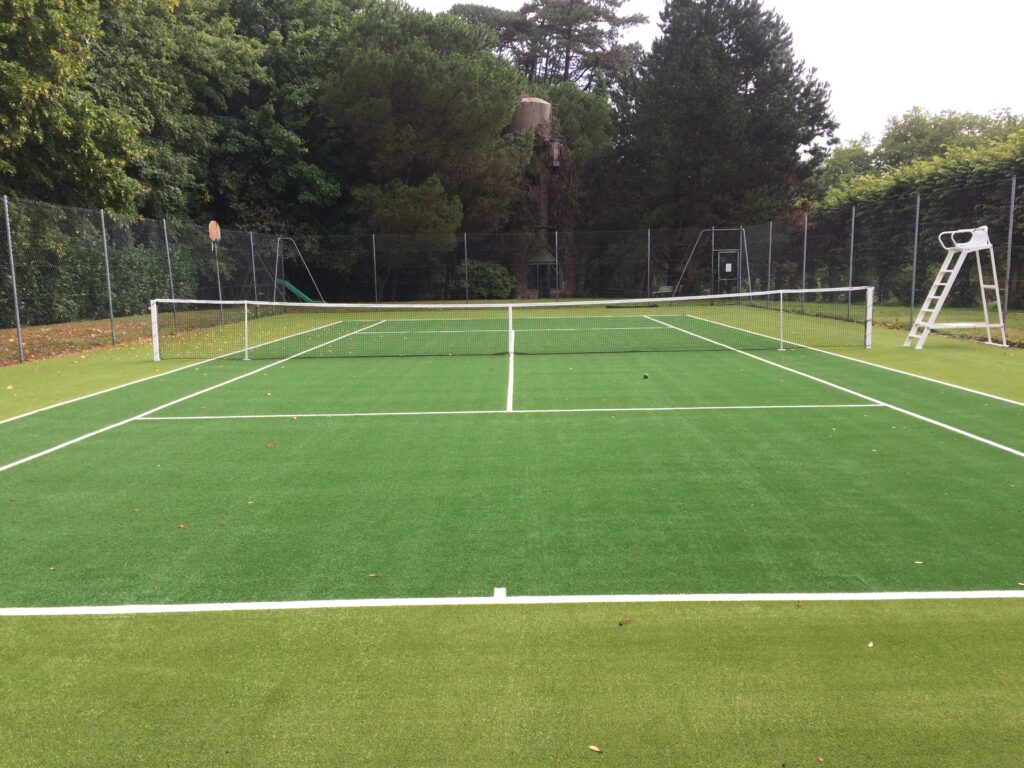 Terrain de tennis extérieur synthétique entouré d'arbres.