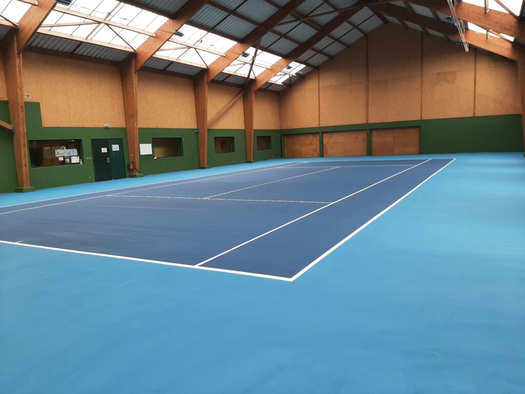 Court de tennis intérieur, surface bleue, structure bois.