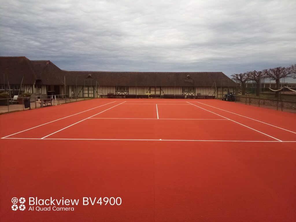 Terrain de tennis rouge vide avec bâtiments.